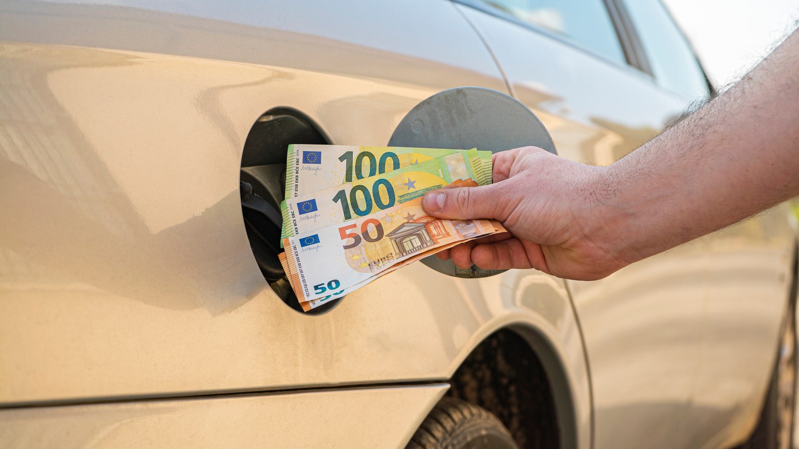 Hand, die Euroscheine in den Tankstutzen eines Autos steckt